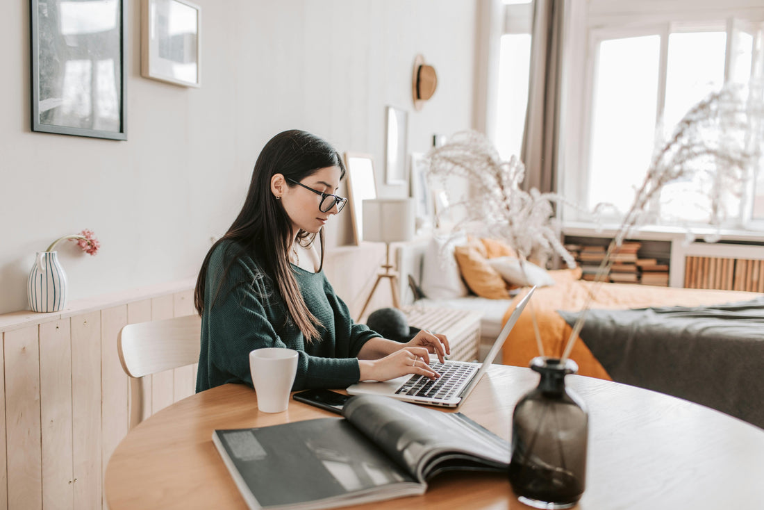 A photo of a woman sat at a table typing on her macbook.